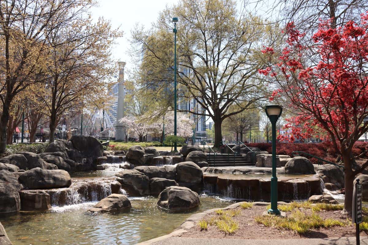 A small landscaped park with rocks, waterfalls, trees, and a pathway, with buildings visible in the background—an inviting spot often highlighted in any atlanta travel guide.