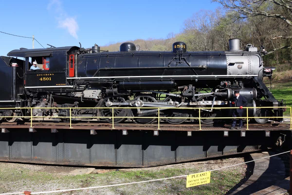 Black steam locomotive numbered 4501 sits on a turntable outdoors with a yellow safety sign in the foreground and a person standing nearby.