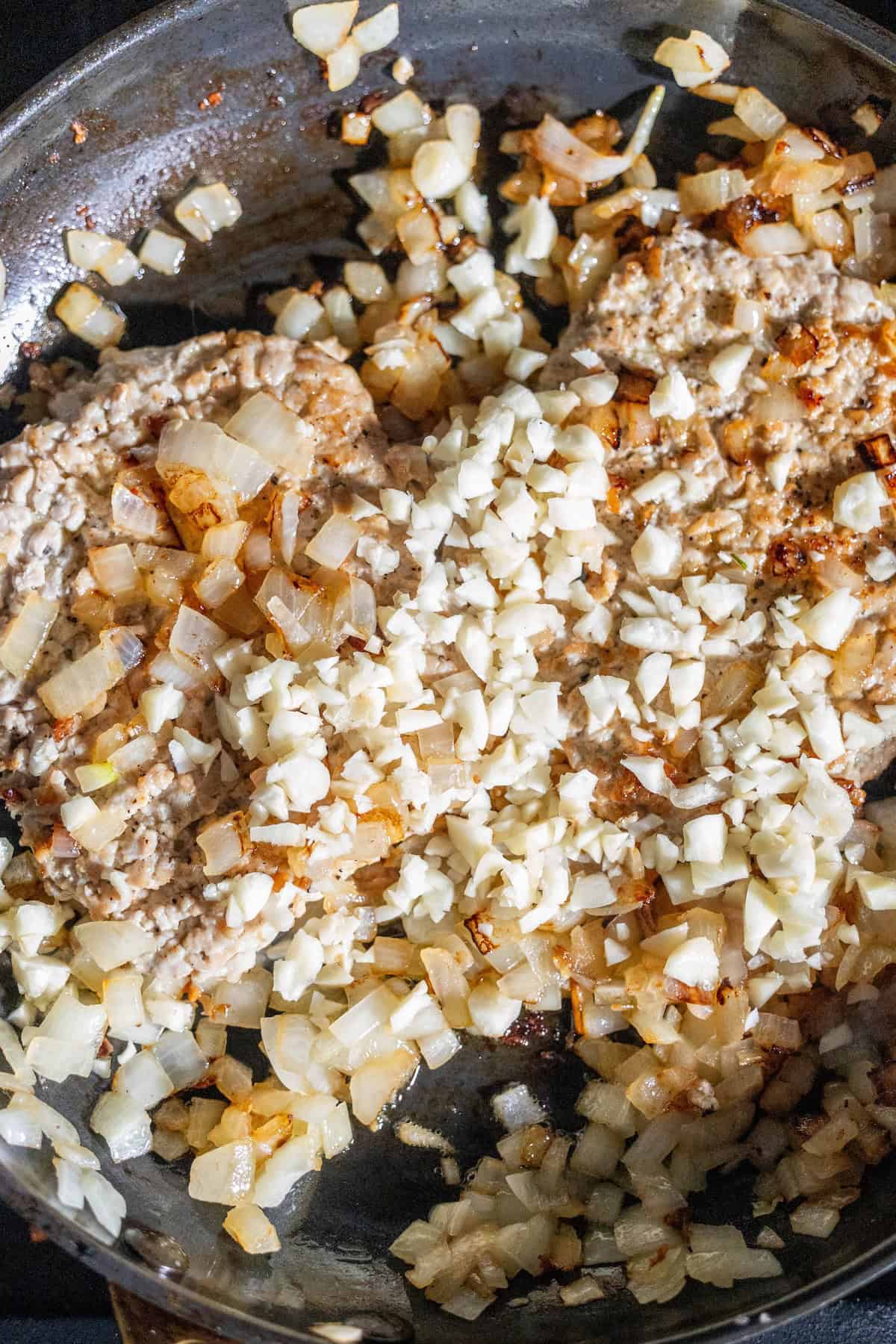 Chopped onions and garlic sautéing with browned ground meat in a skillet, creating the savory base for a classic Pork Swiss Steak.