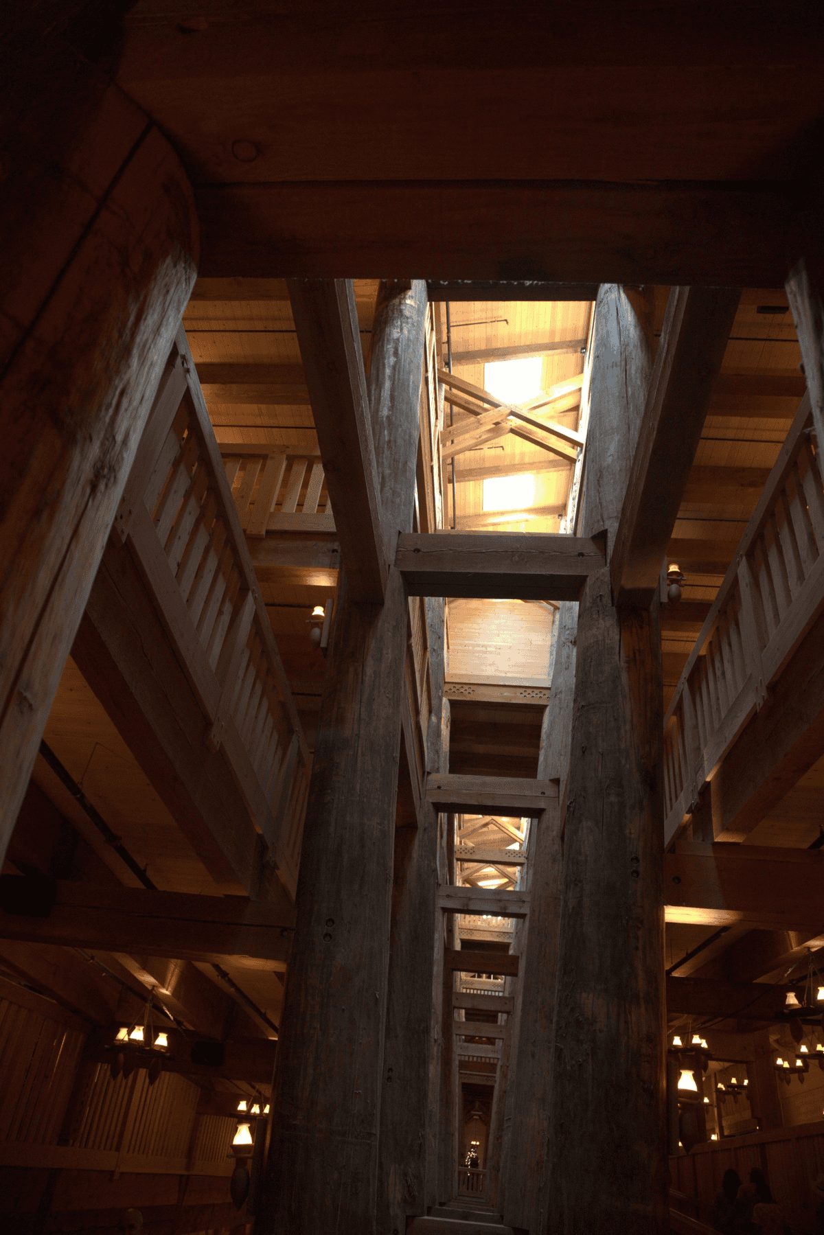 Interior view of a large wooden structure with thick beams, multiple levels, railings, and natural light coming through openings above.