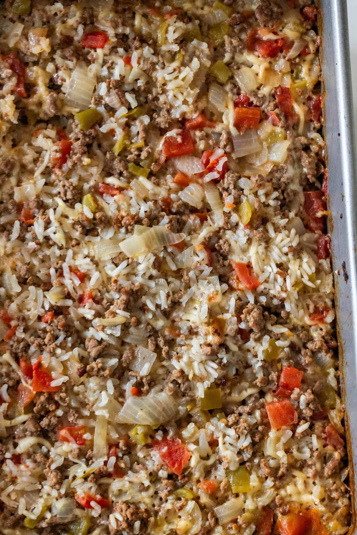 A close-up of a casserole dish filled with baked dirty rice, featuring ground meat, diced tomatoes, onions, and bell peppers. This baked rice is a comforting twist on the classic Dirty Rice Recipe.