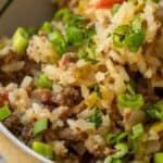 Close-up of a Baked Dirty Rice casserole with ground meat, topped with chopped green onions and herbs.