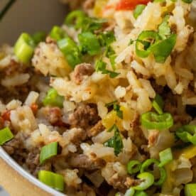 Close-up of a Baked Dirty Rice casserole with ground meat, topped with chopped green onions and herbs.