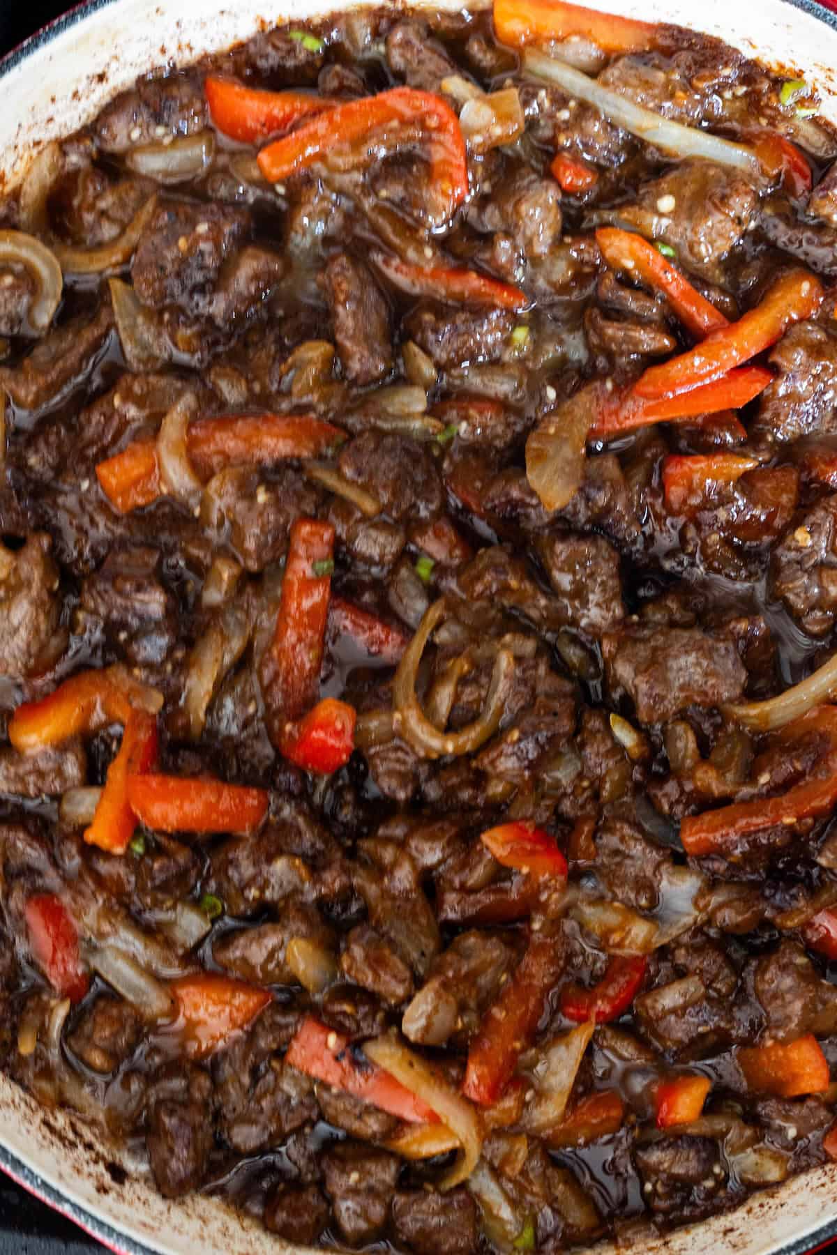 A close-up of pepper and beef stir fry: tender beef strips, red bell peppers, and onions coated in a dark sauce—just like your favorite better than takeout beef stir fry.