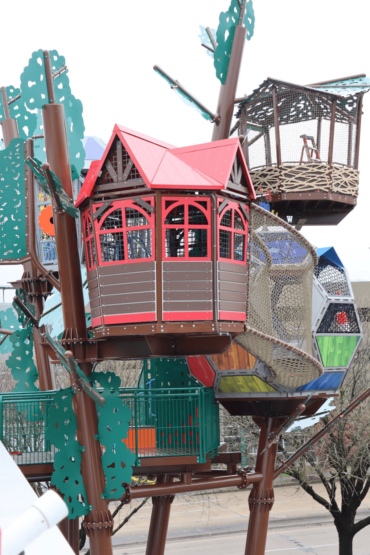 Elevated, colorful treehouse structures connected by netted bridges and walkways, set among simulated tree trunks in an outdoor play area.