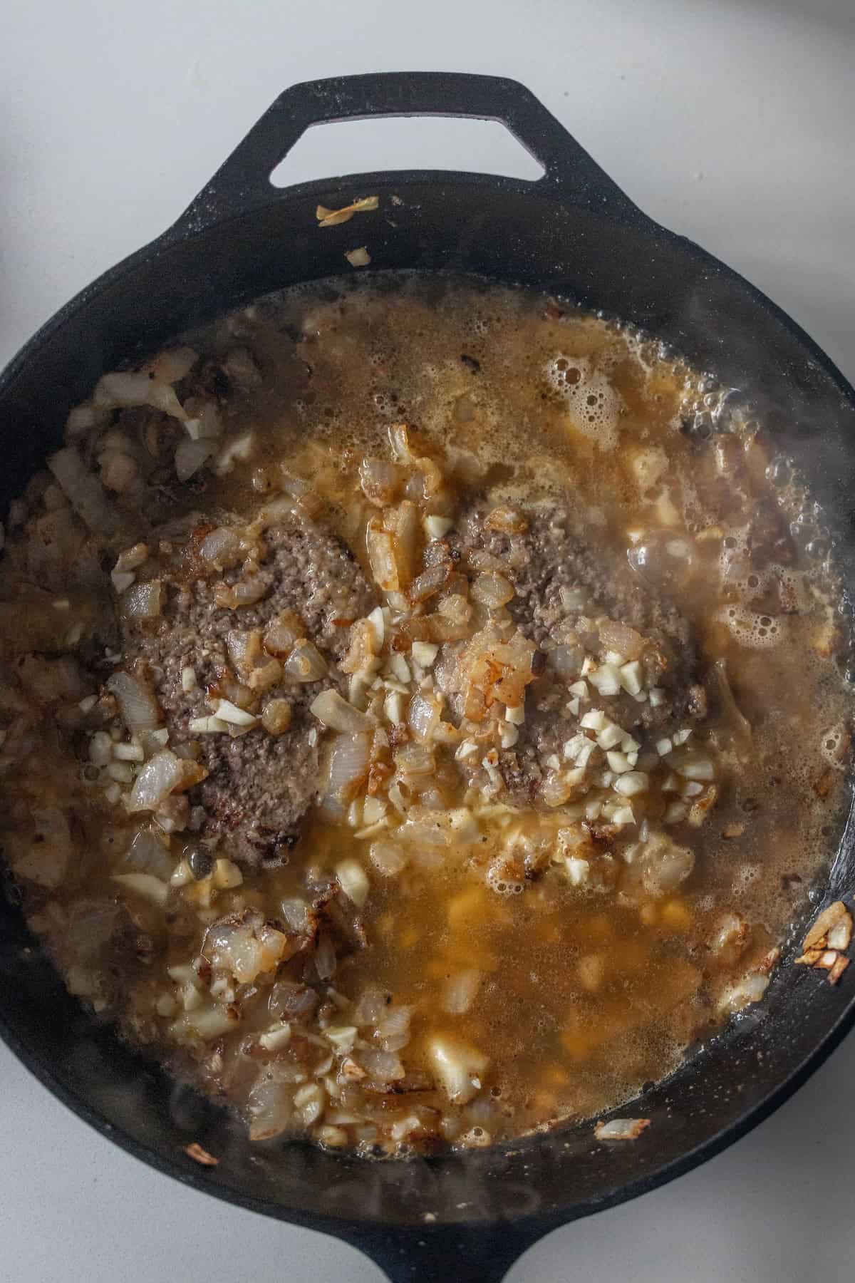 A cast iron skillet with cooked ground beef, chopped onions, and savory gravy simmering together—perfect for a comforting Country Steak Recipe.