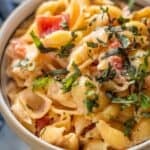 A close-up of shell pasta mixed with a creamy sauce, diced tomatoes, and topped with chopped fresh herbs.