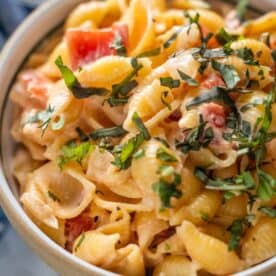 A close-up of shell pasta mixed with a creamy sauce, diced tomatoes, and topped with chopped fresh herbs.