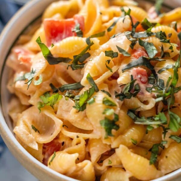 A close-up of shell pasta mixed with a creamy sauce, diced tomatoes, and topped with chopped fresh herbs.