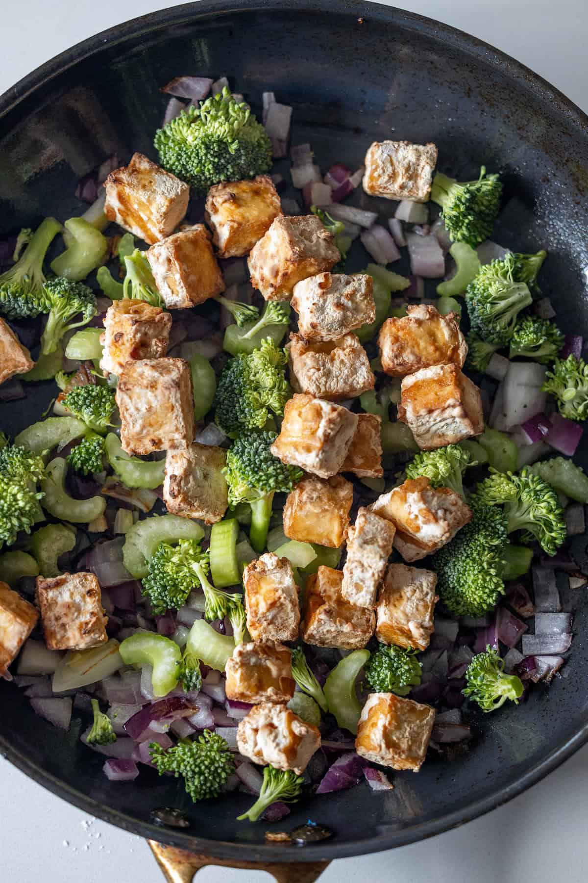A skillet with crispy tofu cubes, sautéed broccoli, celery, and red onions makes a vibrant stir fry.