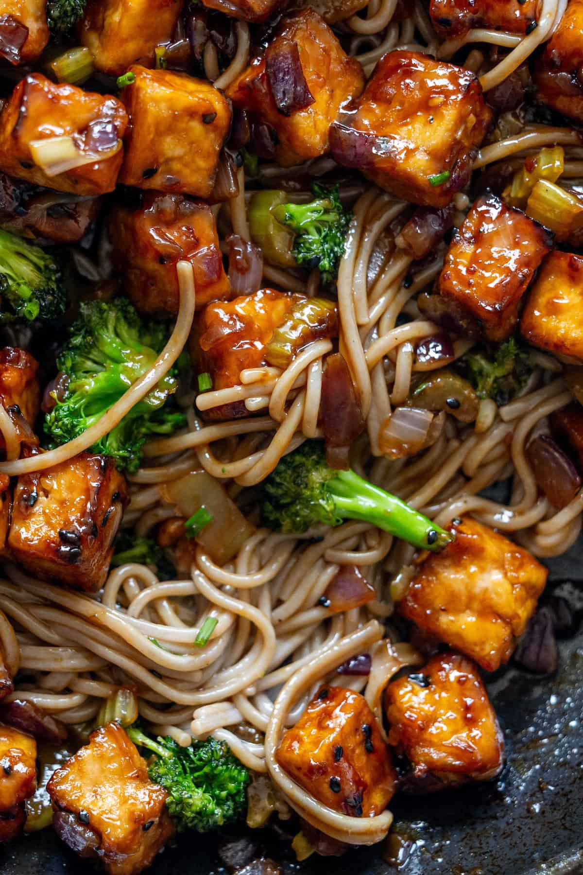 Stir-fried soba noodles with broccoli, crispy tofu cubes, and chopped onions coated in a glossy sauce.