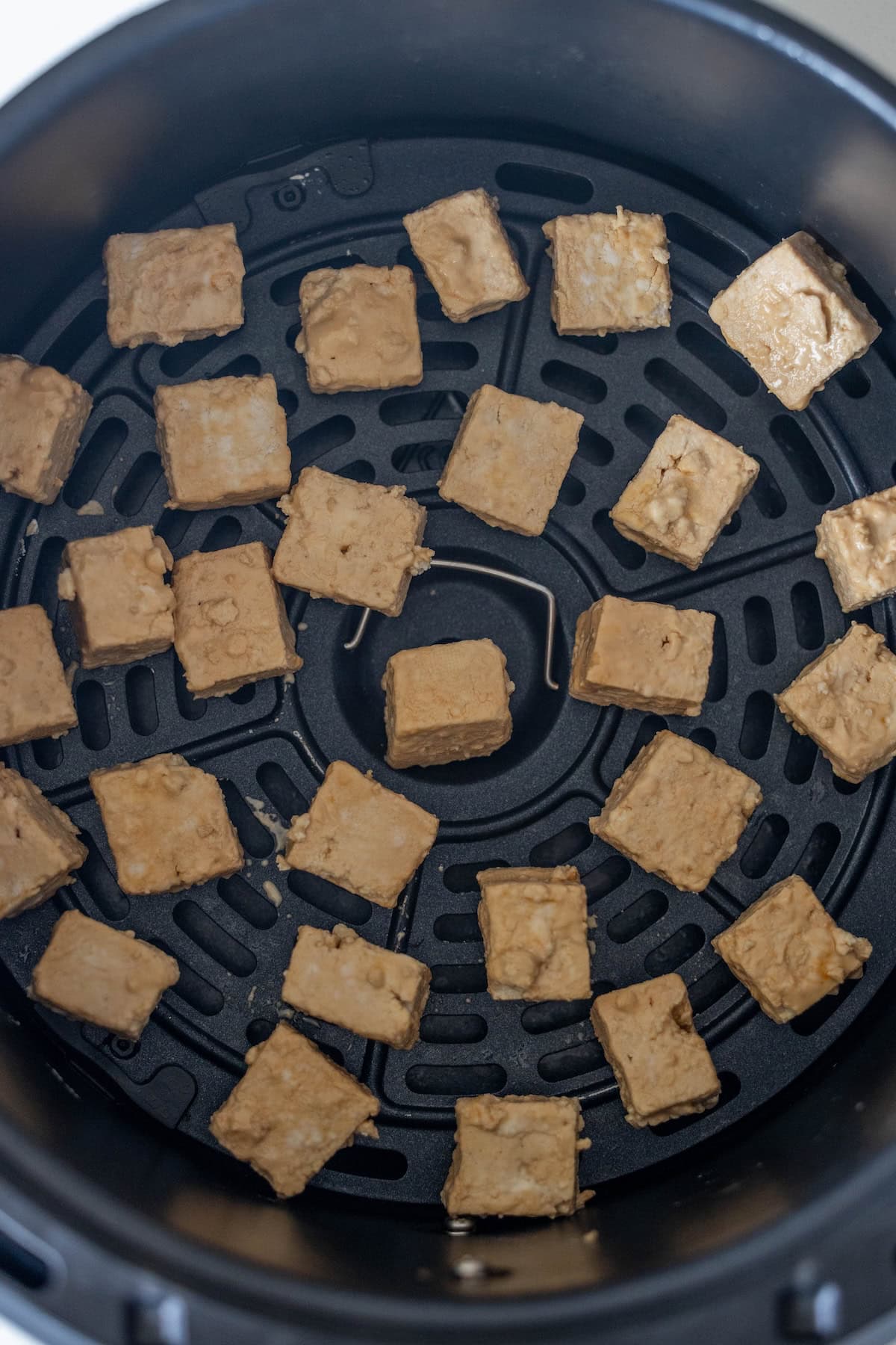Crispy tofu cubes arranged in a single layer inside an air fryer basket, ready to be cooked—perfect for adding to your favorite stir fry or serving alongside soba noodles.