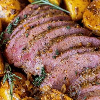 Sliced seasoned roast beef garnished with fresh herbs, surrounded by roasted potatoes—a classic addition to your Saint Patrick's Day favorite recipes.