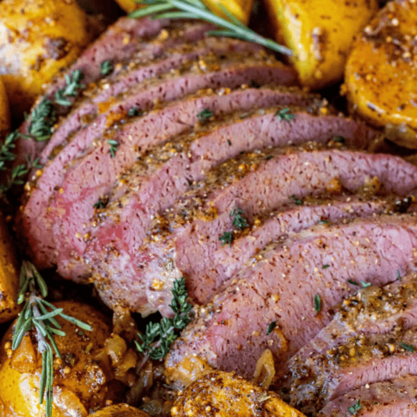 Sliced seasoned roast beef garnished with fresh herbs, surrounded by roasted potatoes—a classic addition to your Saint Patrick's Day favorite recipes.