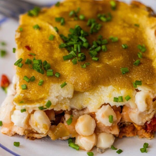 A close-up of vegan enchilada pie topped with chopped chives, showing layers of white hominy, savory sauce, and a golden crust.