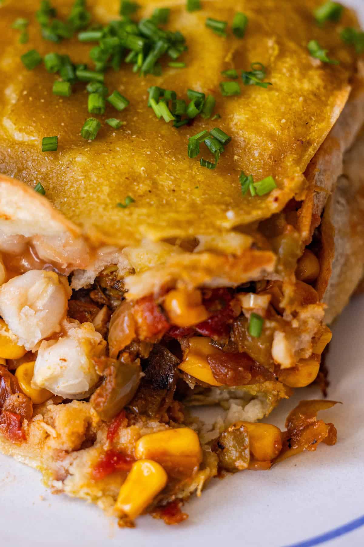 Close-up of a cheesy Vegan enchilada pie filled with corn, vegetables, and beans, topped with sauce and chopped chives on a white plate—a delicious vegan recipe for any meal.