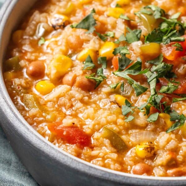 A close-up of a bowl of vegan soup, featuring rice, chickpeas, corn, tomatoes, and chopped cilantro on topโperfect for fans of hearty vegan charro bean or classic rice soup.