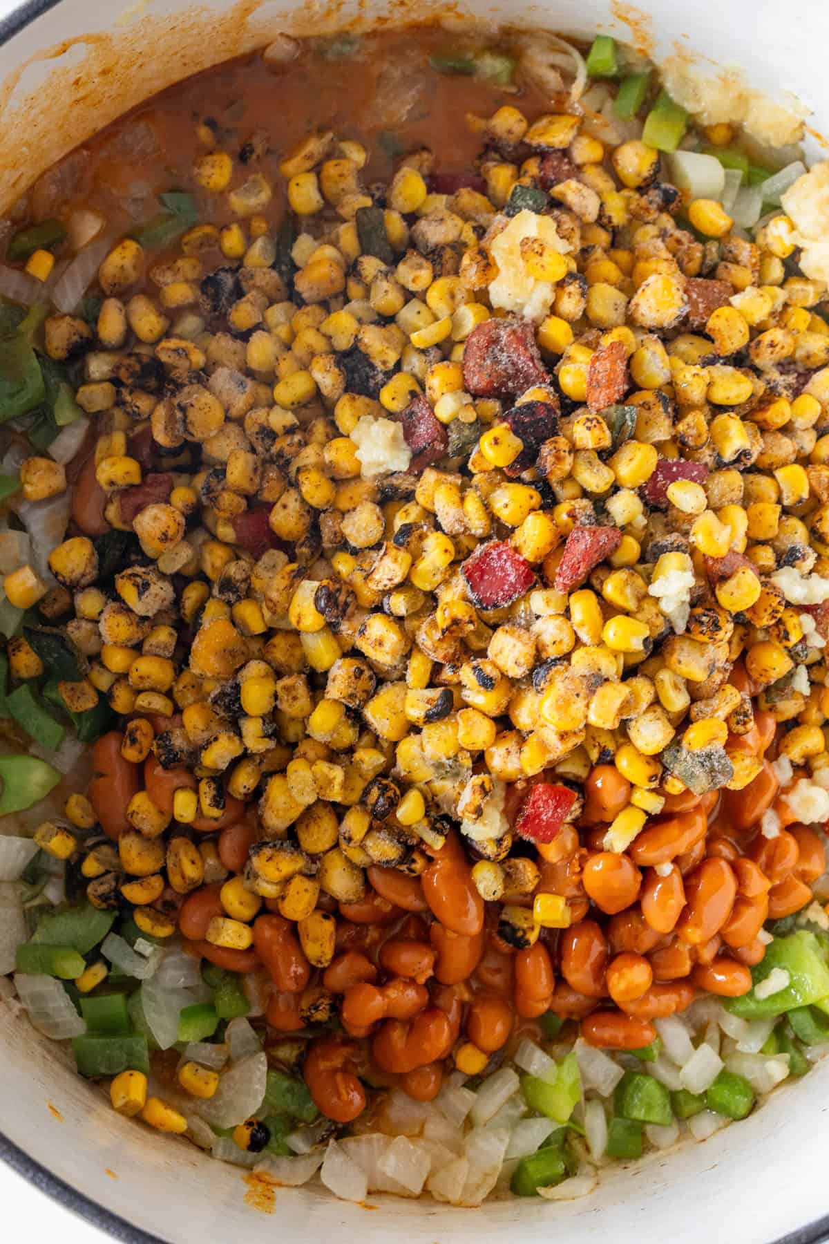 A close-up of a pot containing roasted corn, pinto beans, chopped green bell pepper, and diced onions in a tomato-based sauce—perfect for a hearty Vegan Charro Bean soup.