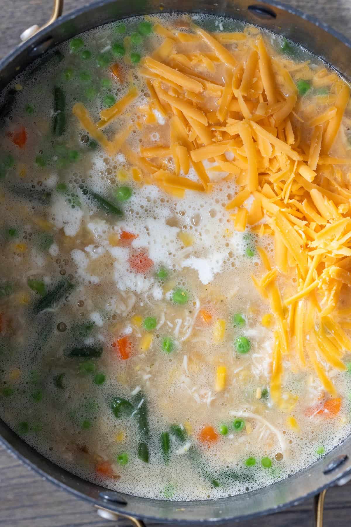A pot of cheesy corn chowder with mixed vegetables, shredded chicken, crispy bacon, and melted cheddar cheese on top.