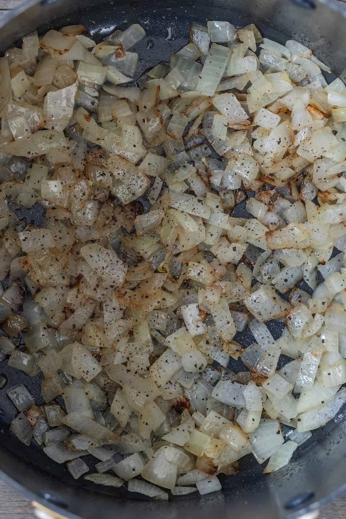Chopped onions saut&eacute;ing in a pan with bacon, lightly browned and sprinkled with visible seasoning.