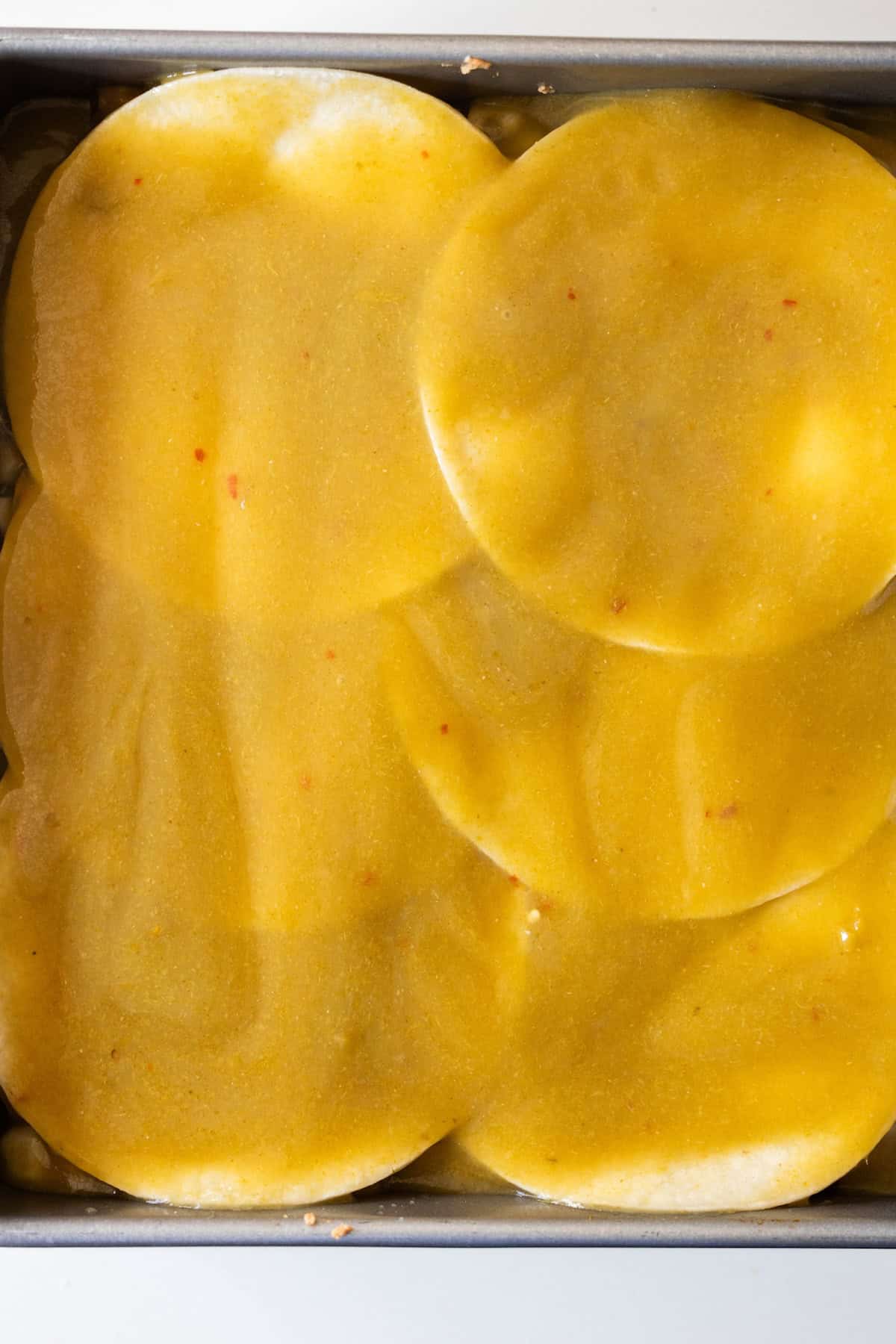 Close-up of several round pasta sheets layered in a baking dish, covered with a yellow vegan sauce.