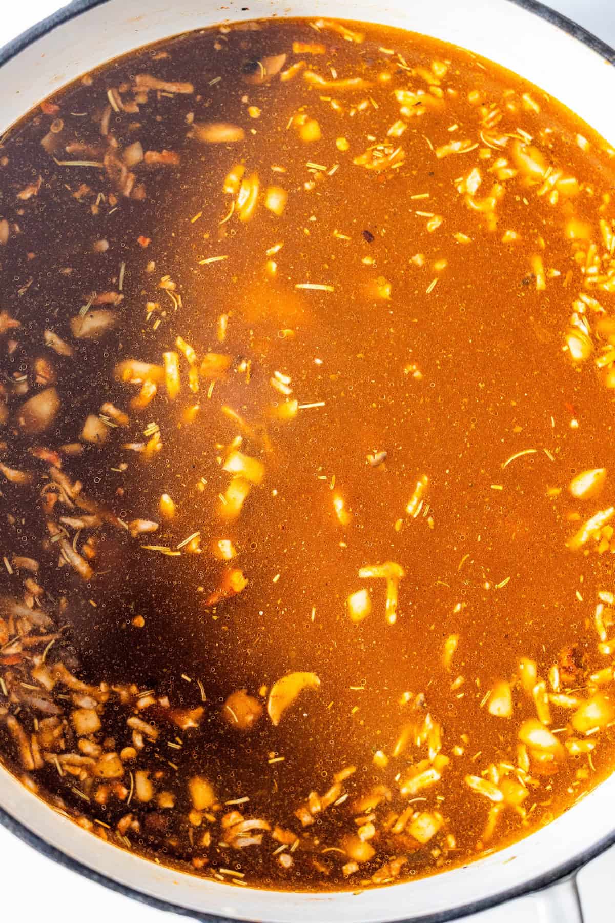 A close-up view of a pot filled with brown vegan broth containing chopped onions, herbs, and seasonings&mdash;an inviting base for a hearty vegan soup.