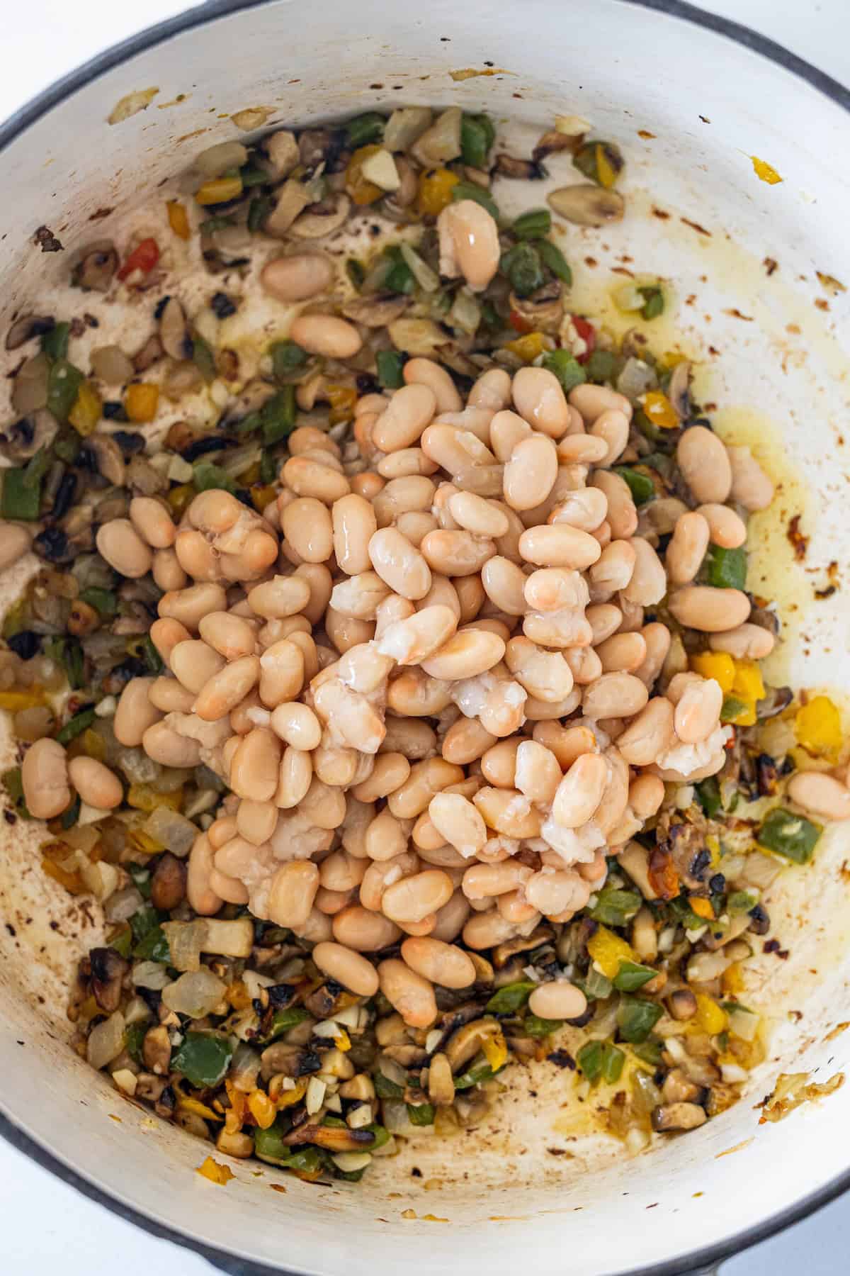 Vegan Soup with white beans, chopped peppers, onions, and seasonings simmering in a large white pot&mdash;partially cooked and ready for mixing.