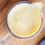 A glass measuring cup filled with creamy yellow sauce, viewed from above, on a wooden surface.
