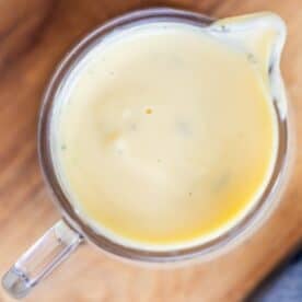 A glass measuring cup filled with creamy yellow sauce, viewed from above, on a wooden surface.