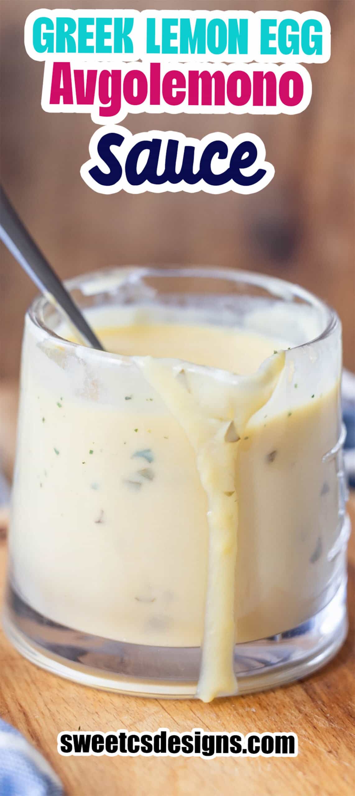 A glass cup filled with Greek avgolemono sauce, some of the silky avgolemono sauce dripping down the side, and a spoon nestled inside.