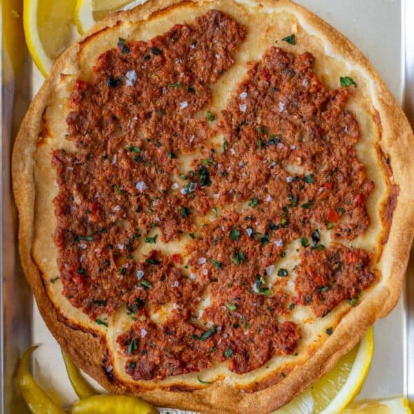 Easy Lahmajoun is a round flatbread topped with minced meat, herbs, and spices, served with lemon wedges and green peppers on the side.