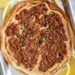 Easy Lahmajoun is a round flatbread topped with finely minced meat, herbs, and spices, served with lemon wedges on the side.