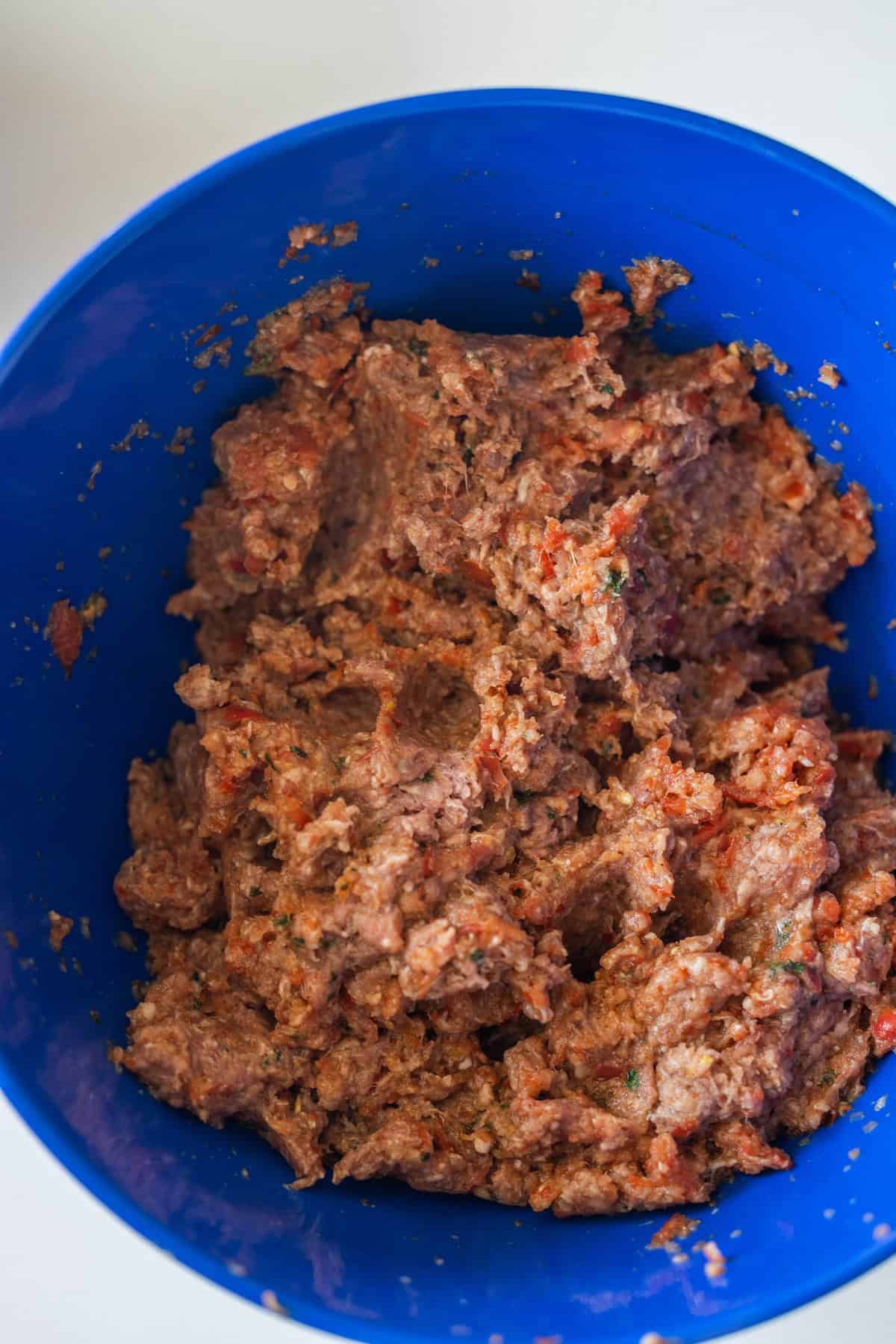 Ground meat mixed with chopped vegetables and seasonings in a blue bowl, perfect for making Easy Lahmajoun.