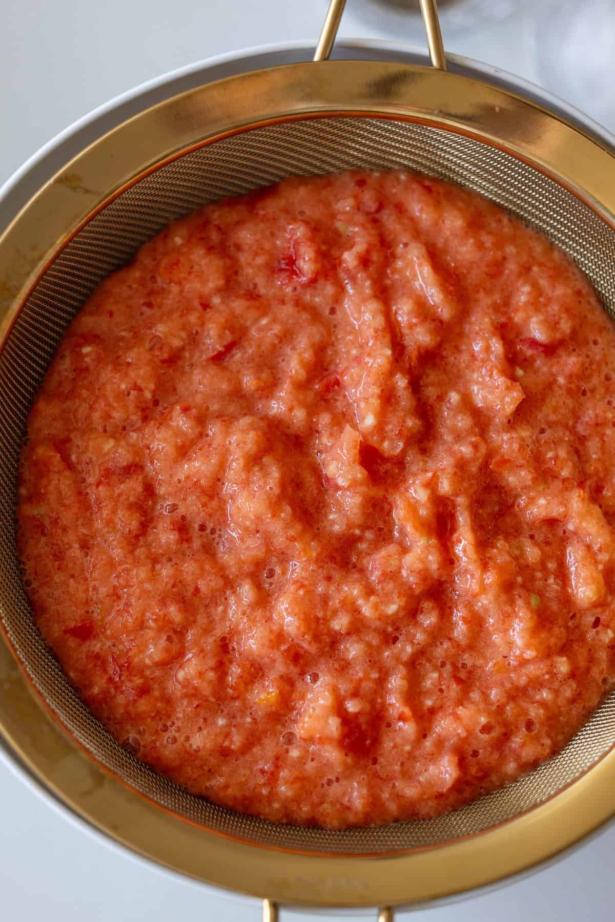 A close-up of blended tomato pulp in a fine mesh strainer, with liquid beginning to drain below—an essential step for making Easy Lahmajoun.