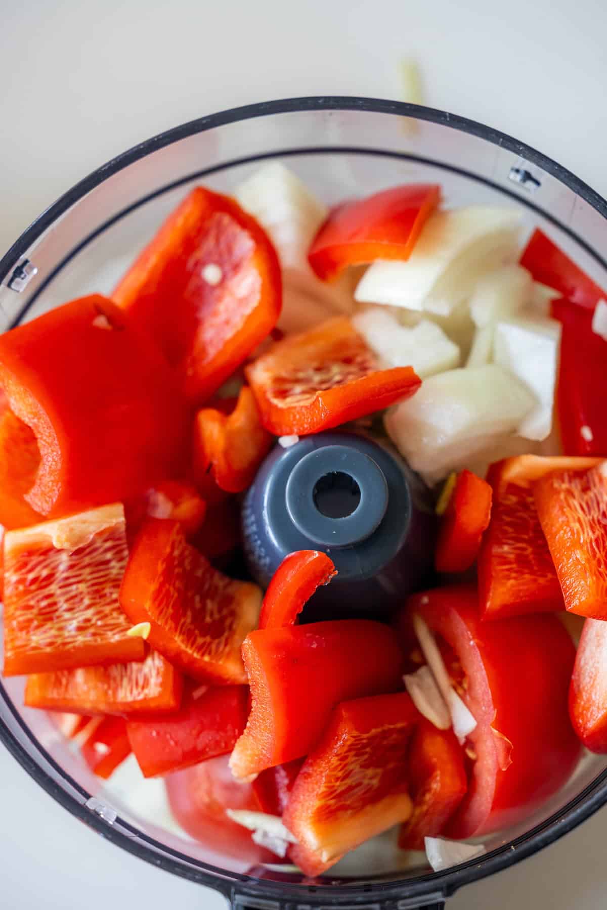 Chopped red bell peppers and onions in a food processor bowl, ready for processing—perfect for making Easy Lahmajoun.