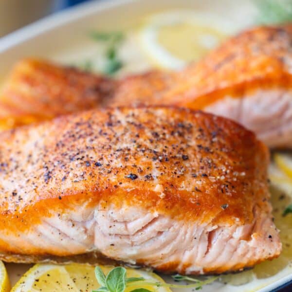 Close-up of Pan Fried Salmon filets on a bed of lemon slices, garnished with fresh herbs.