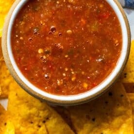 A bowl of chunky roasted salsa surrounded by yellow corn tortilla chips.