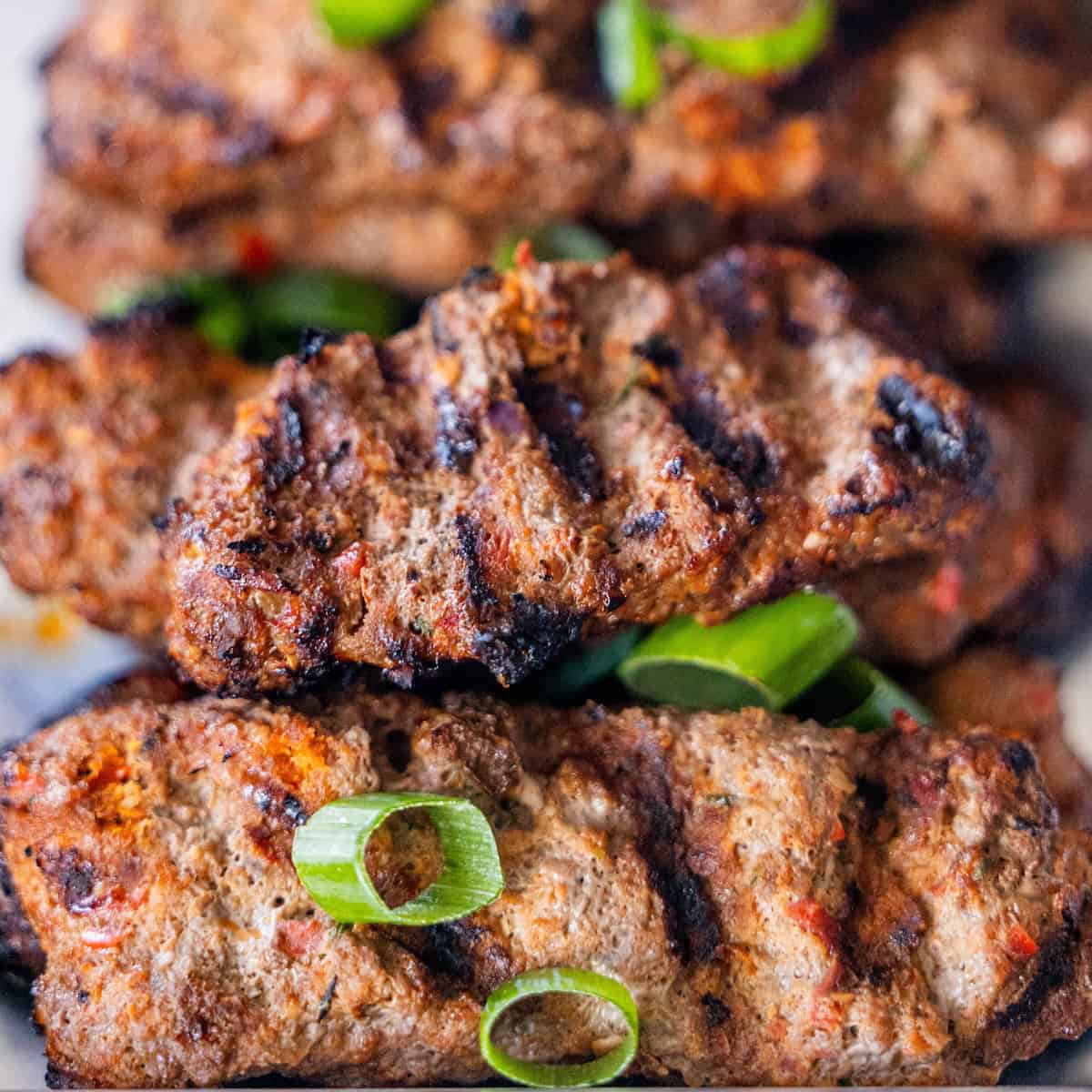 Armenian kebabs of spiced meat with visible grill marks, garnished with chopped green onions.