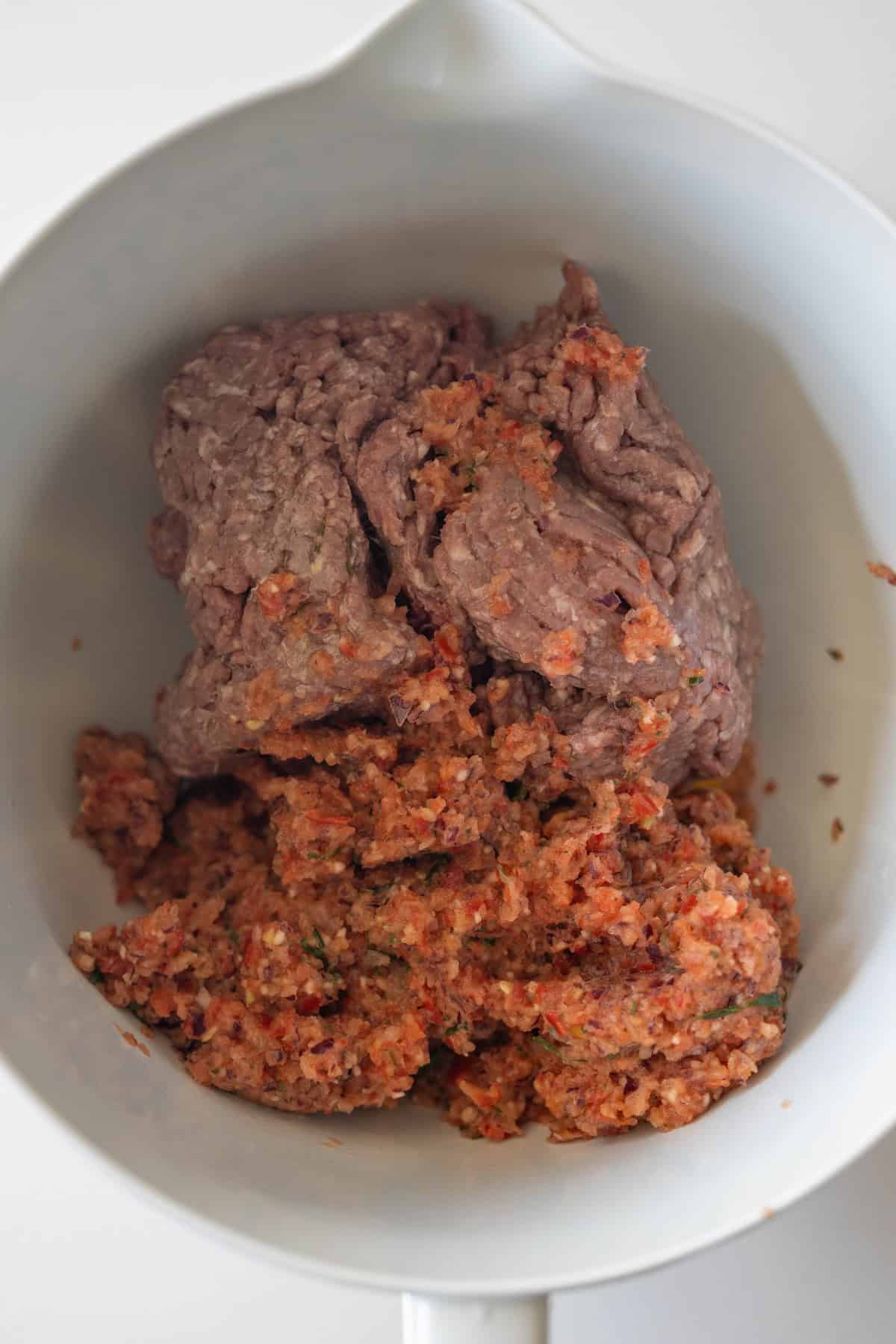 Ground beef and a mixture of finely chopped vegetables or seasonings come together in a white mixing bowl, perfect for preparing flavorful Armenian spiced meat kebabs.
