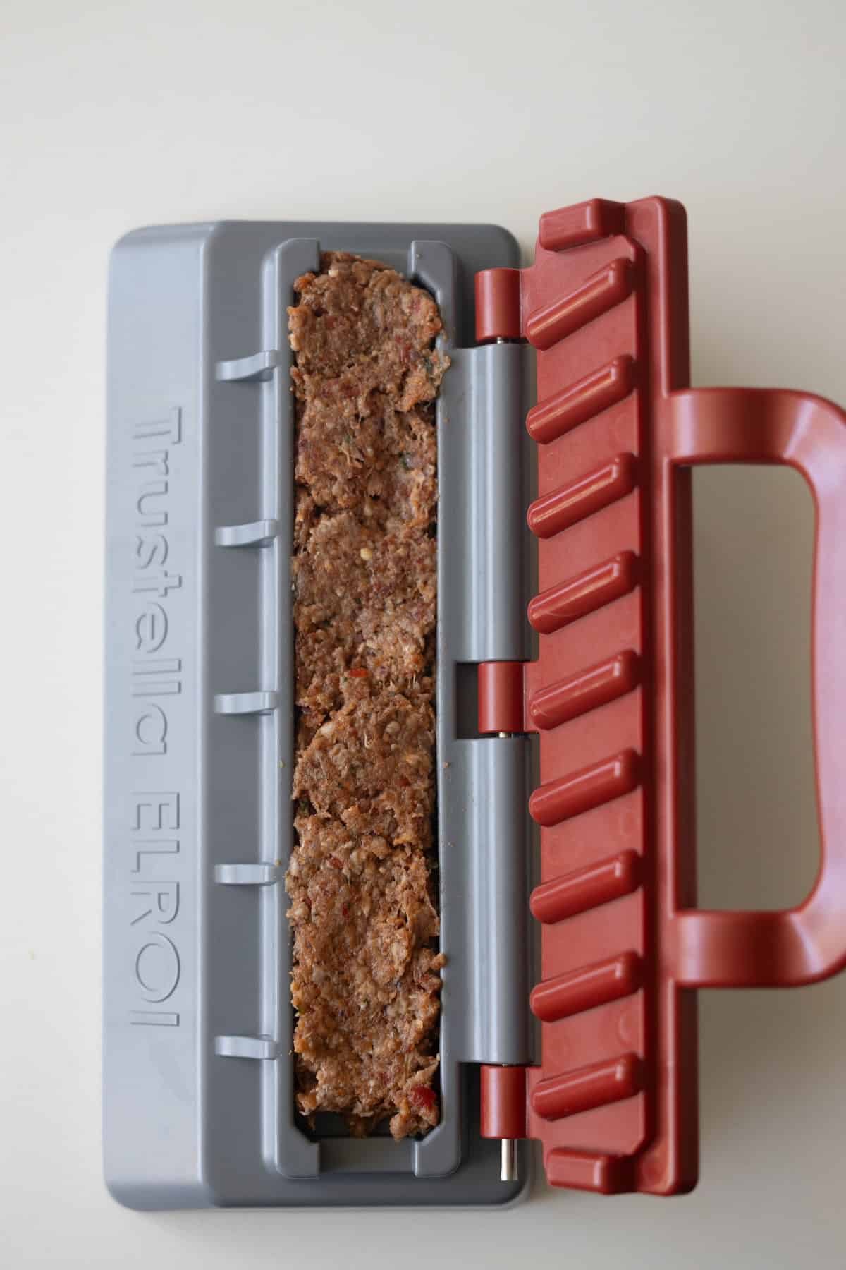 A close-up of spiced meat mixture packed inside a gray and red plastic mold labeled "Trustella ELROI" on a light surface, perfect for making Armenian kebabs.