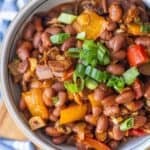 A bowl of delicious Mexican beans mixed with diced bell peppers, onions, and topped with chopped green onions.