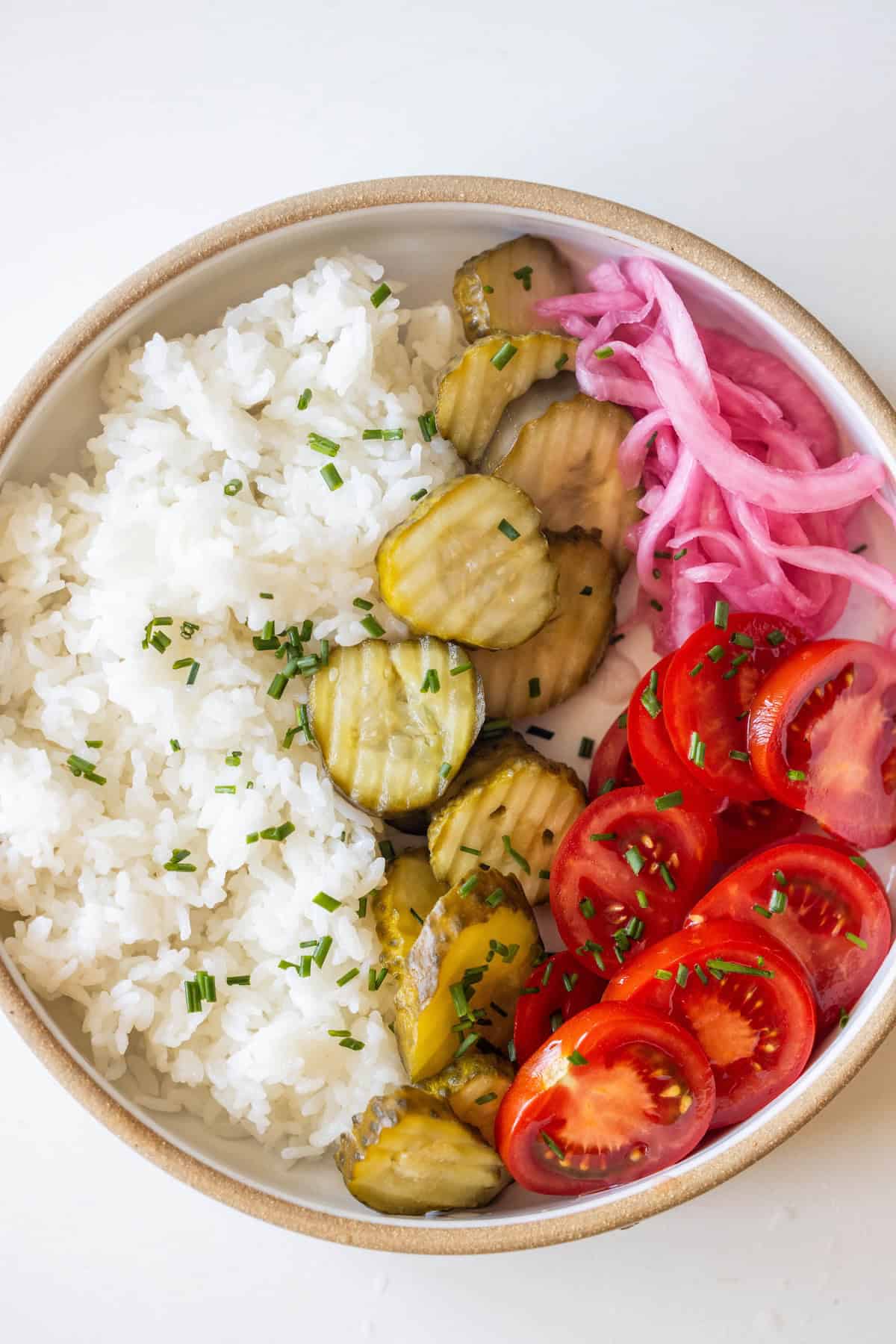 A fresh take on burger bowls: white rice topped with sliced pickles, halved cherry tomatoes, pickled red onions, and a sprinkle of chopped chives.
