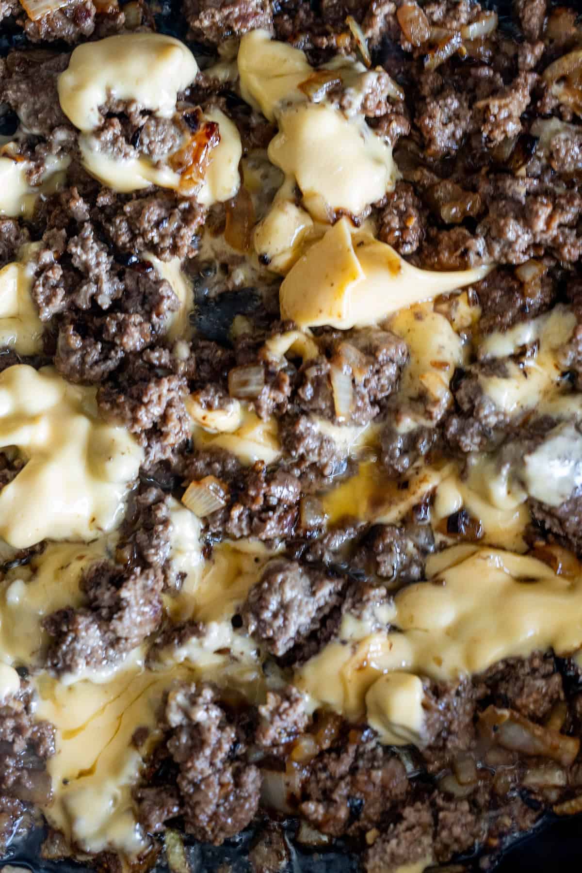 Cooked ground beef with melted cheese and sautéed onions in a skillet—just what you need to master a classic Chopped Cheese Sandwich Recipe or learn how to make chopped cheese at home.