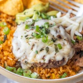 Enjoy our Burger Bowls: a hamburger patty topped with melted cheese, chopped green onions, and zesty green chile served over seasoned rice, with chips, guacamole, and shredded cheese on the side.