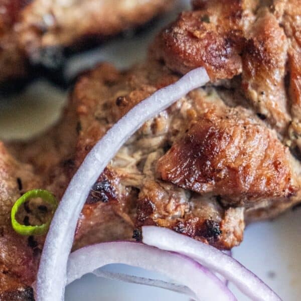 Close-up of onion marinated pork with visible grill marks, garnished with sliced red onions and a green chili pepper.