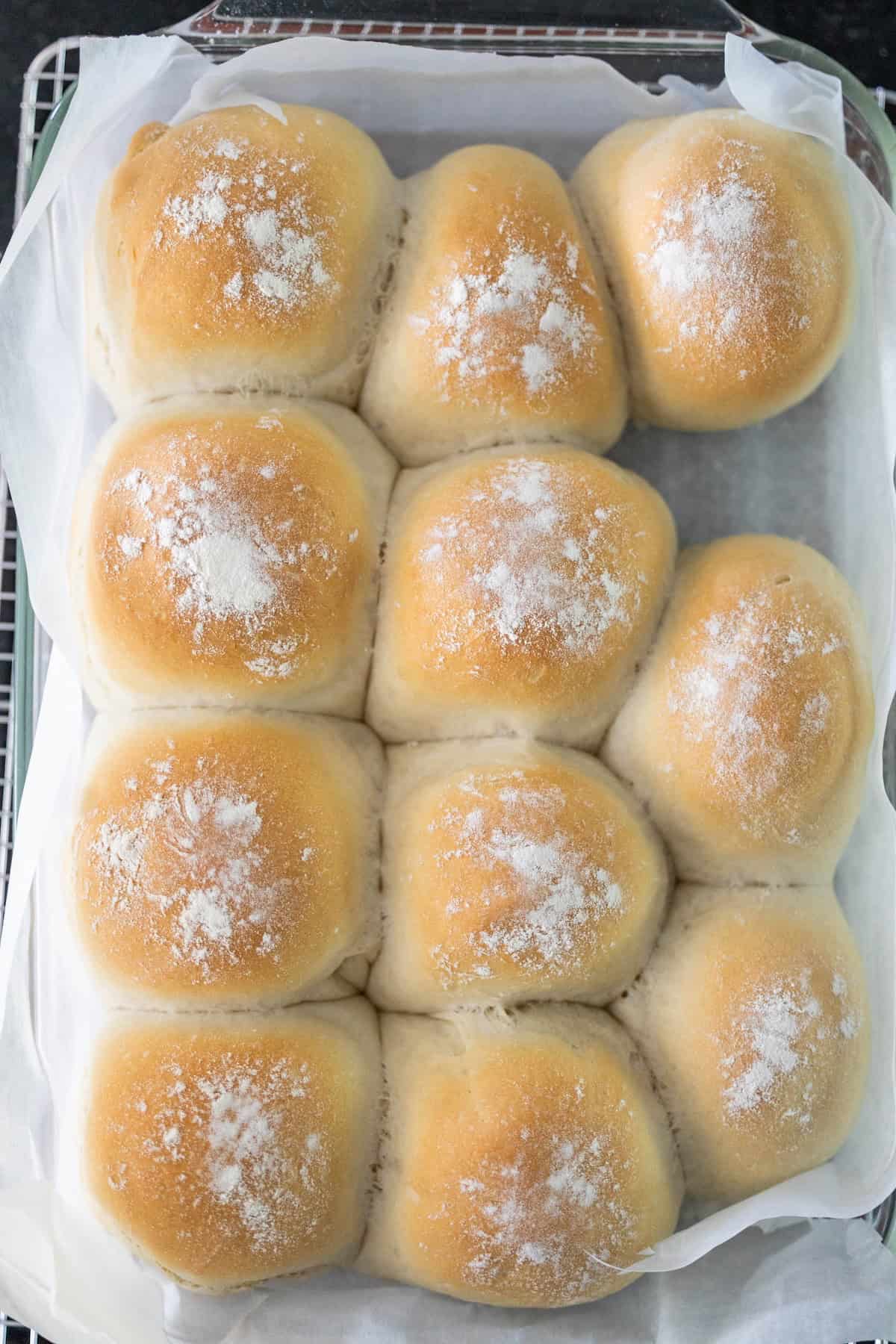 A tray of twelve golden brown Scottish morning rolls dusted with flour, arranged in three rows on parchment paper.