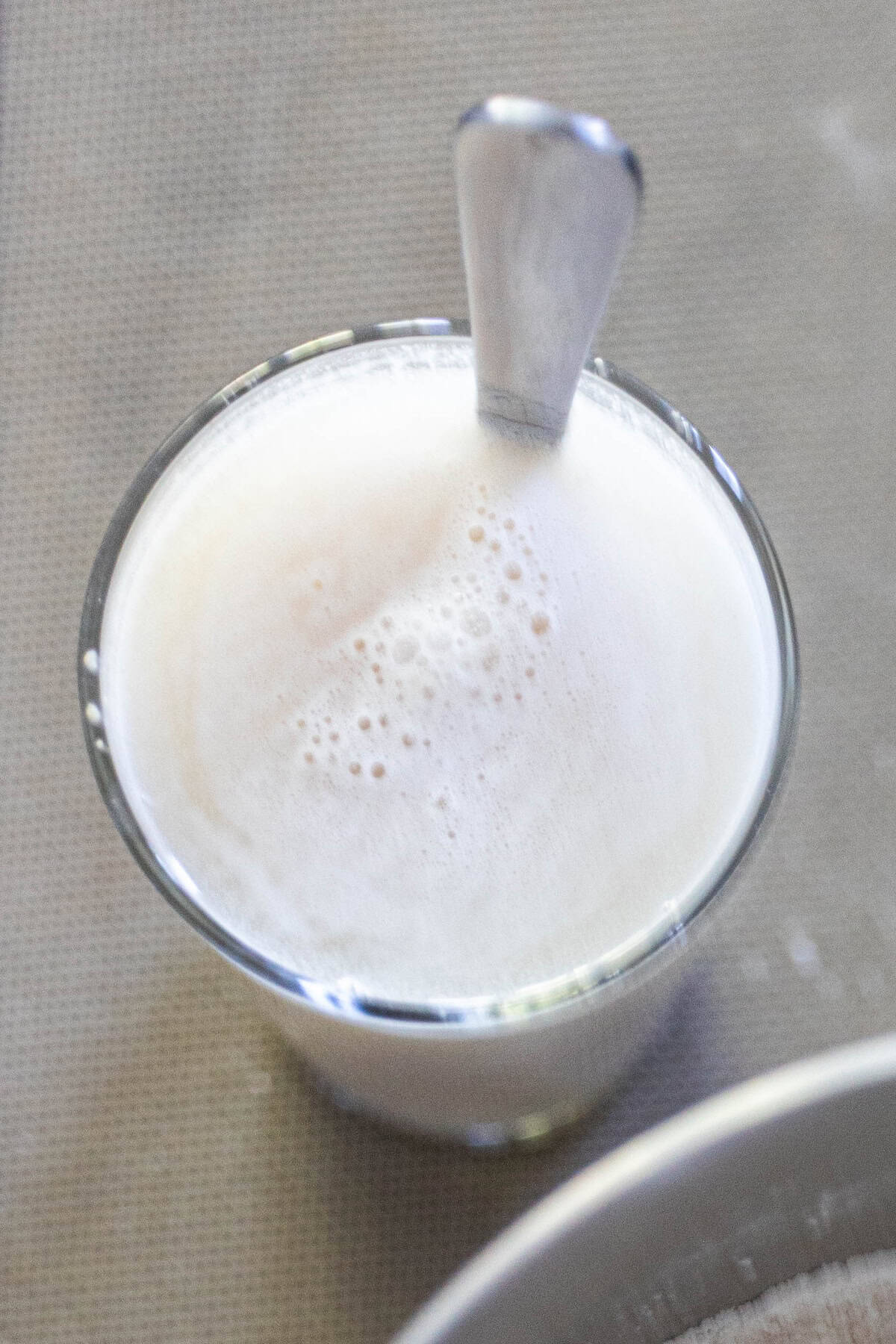 A glass of frothy milk with a metal spoon inside, placed on a light-colored surface, pairs perfectly with freshly baked Scottish Morning Rolls.