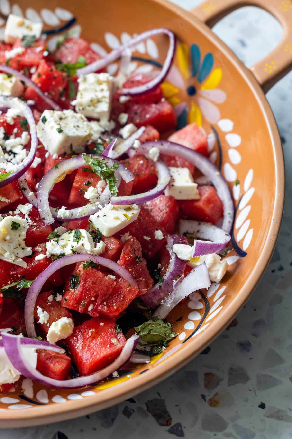 A Watermelon Feta Salad with juicy watermelon cubes, sliced red onions, feta cheese, and fresh mint and basil, served in a decorative ceramic bowl.