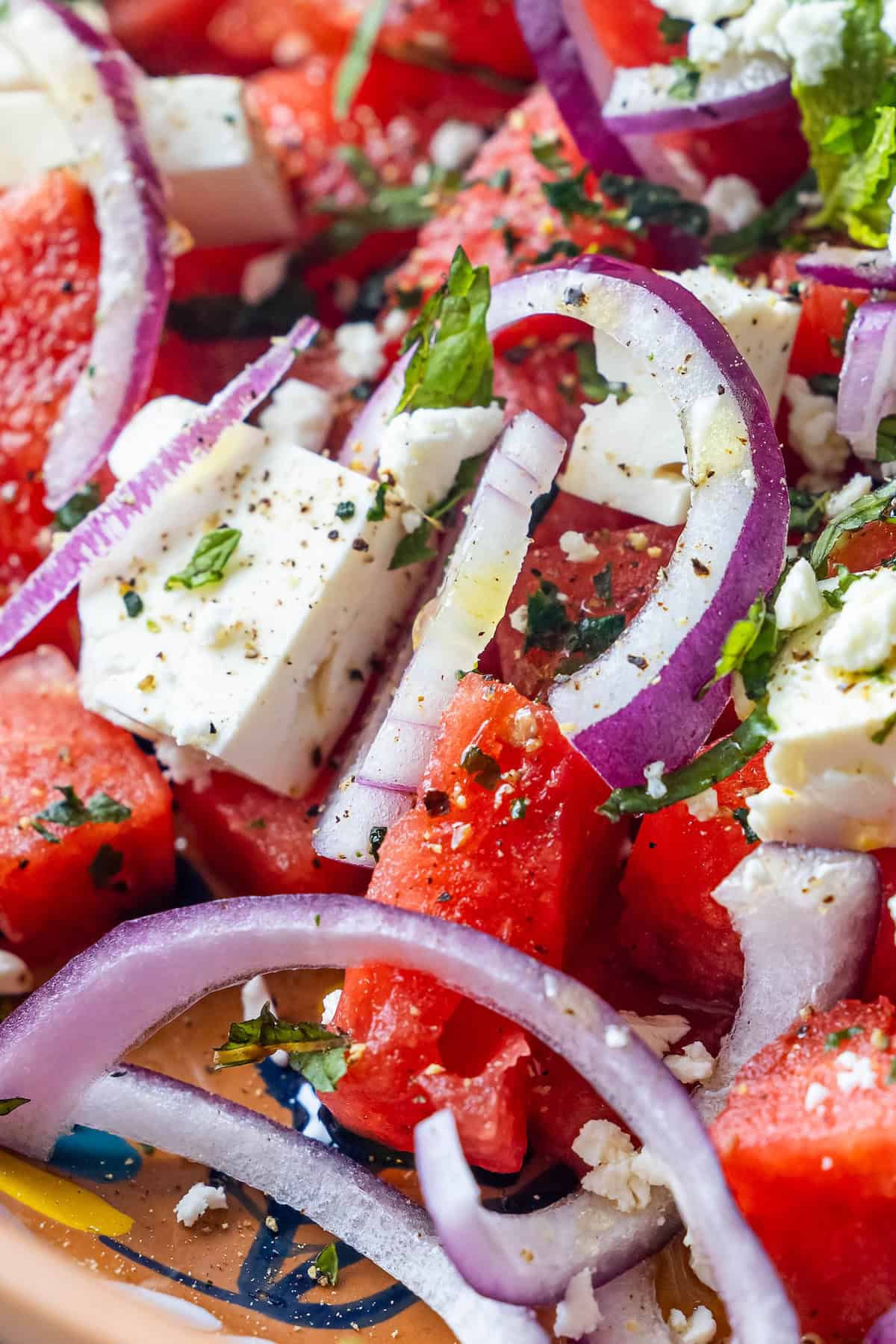 Close-up of a Watermelon Feta Salad with juicy watermelon cubes, feta cheese, sliced red onions, chopped mint and basil, and a sprinkle of black pepper.