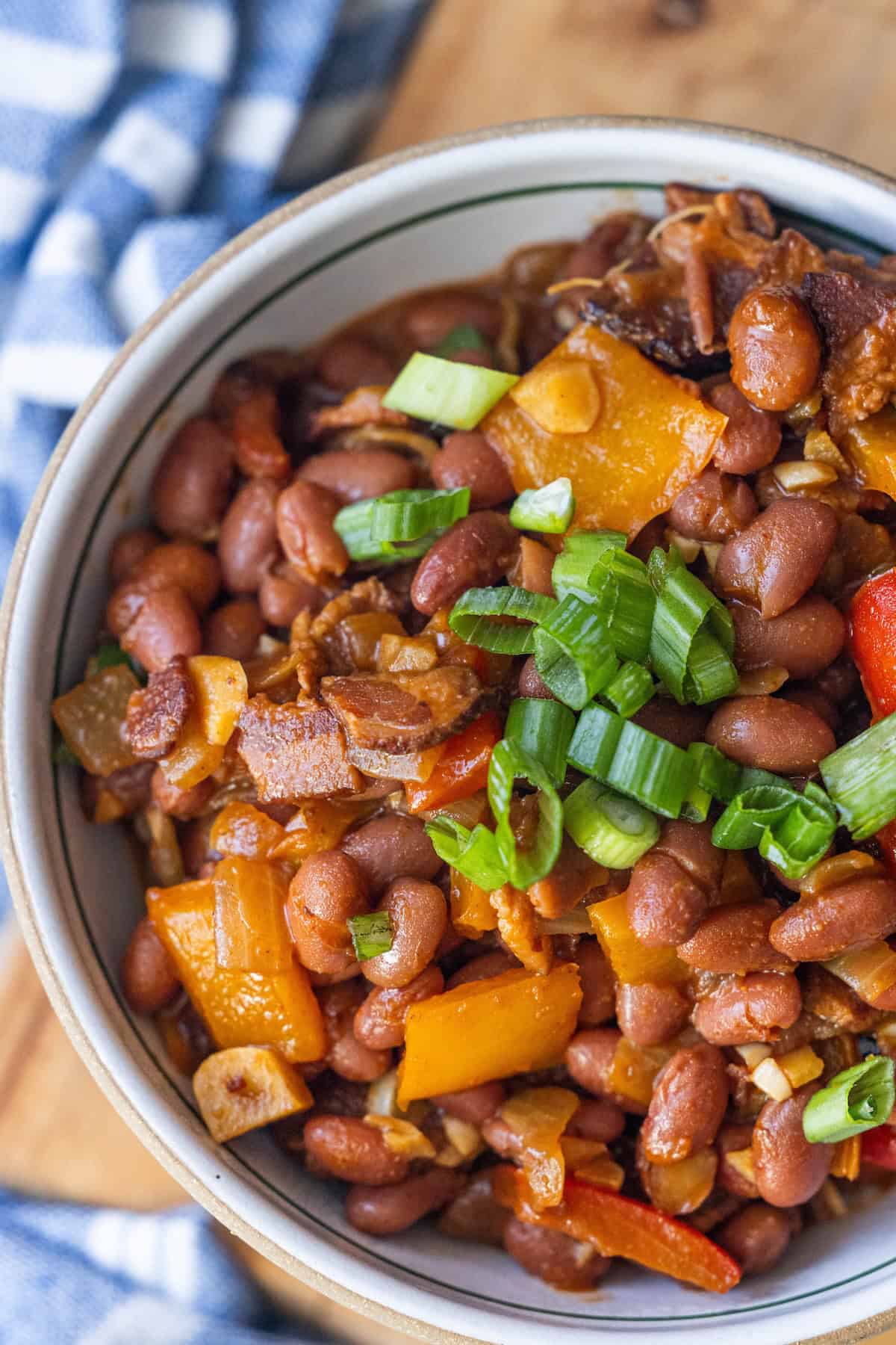 A bowl of cowboy beans mixed with chopped bell peppers, onions, and garnished with sliced green onions.